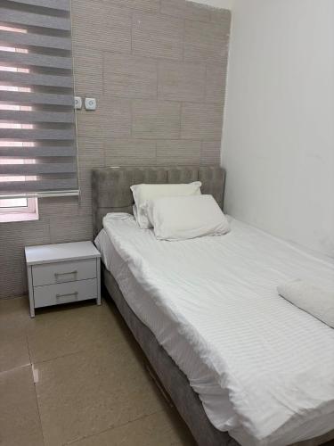 a bed with white sheets and a nightstand next to a window at Laila's studio in Haifa