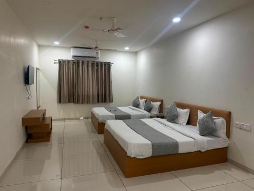a bedroom with two beds and a tv on the wall at Hotel Marigold Vasad in Vāsad