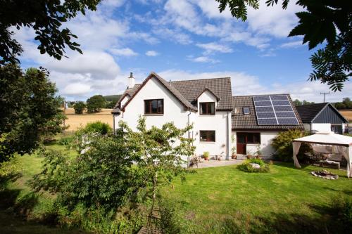 a white house with solar panels on the roof at 5-Bed Highland Lodge - NC500 - Sleeps 10 in Alness