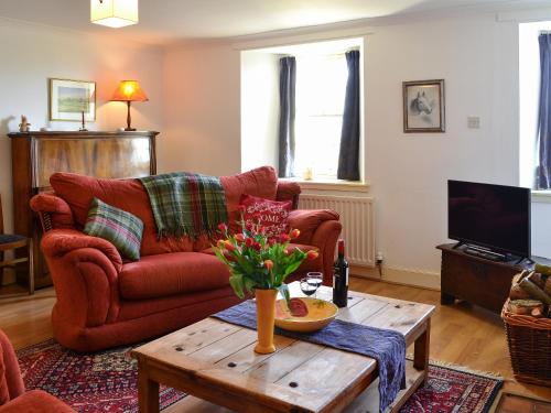 a living room with a red couch and a coffee table at Avenel Cottage in Town Yetholm