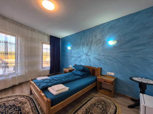 a bedroom with a blue wall with a bed in it at Pensiunea Vraja in Giuleşti