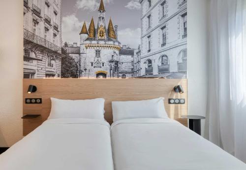 two beds in a room with a picture of a building at B&B HOTEL Bordeaux Mérignac Cadera Aéroport in Mérignac