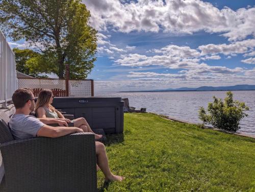 a man and woman sitting on a bench by the water at Chalet #8 Waterfront with Spa, Fireplace, Wifi and AC in Cap-Saint-Ignace