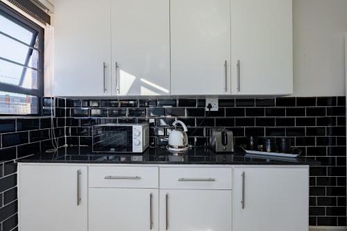 a kitchen with white cabinets and a black tile wall at Safi Self-catering Suite 2 in Bunkers Hill