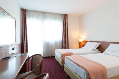 a hotel room with two beds and a desk at Airport Hotel Bergamo in Bagnatica