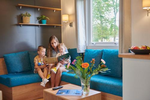 a woman and two children sitting on a blue couch at Siblu Camping Meerwijck in Kropswolde