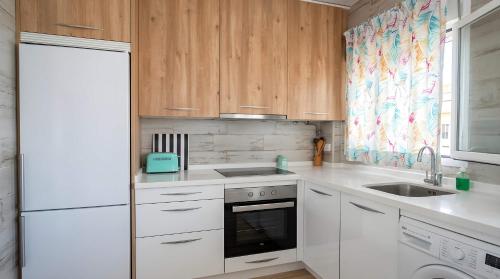 a kitchen with white appliances and wooden cabinets at Apartamento Aguamarina con terraza in Chiclana de la Frontera