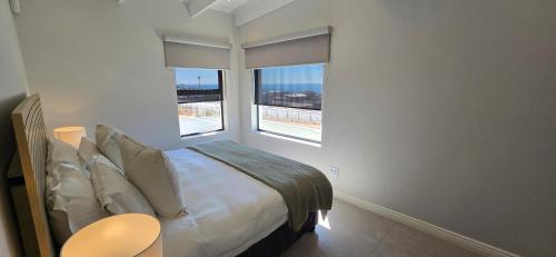 a white bedroom with a bed and two windows at Sage & Salt in St. Helena Bay