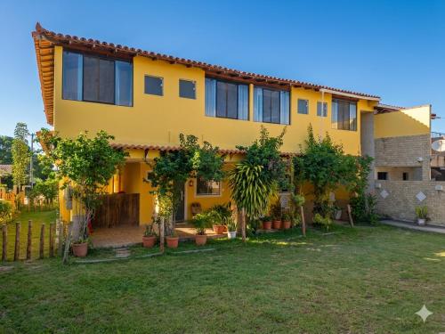 a yellow house with trees in a yard at Guest House Renascer K&W in Cabo Frio