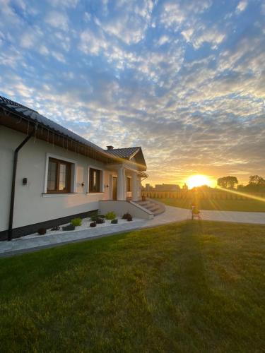 a house with the sunset in the background at Dworek pod Krzyżtoporem Ujazd Agroturystyka- pokoje do wynajęcia in Iwaniska