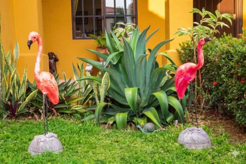 two flamingos standing in the grass in front of a house at Tamarindo Village in San Carlos