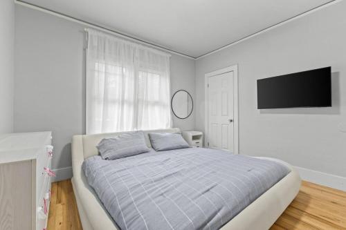 a white bedroom with a bed and a flat screen tv at 2 BR - Fully Equipped Dearborn Home in Dearborn