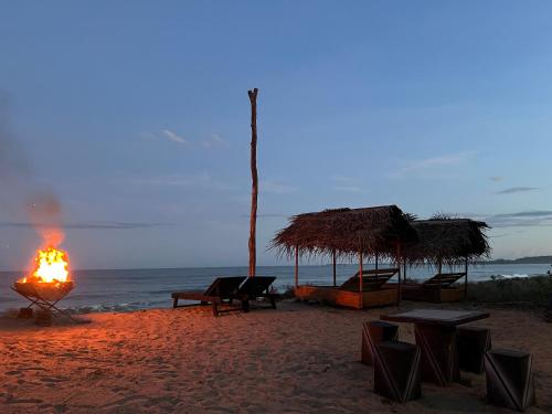 a fire on a beach with tables and umbrellas at Sand Dune Beach Hotel & Surf Camp in Arugam Bay