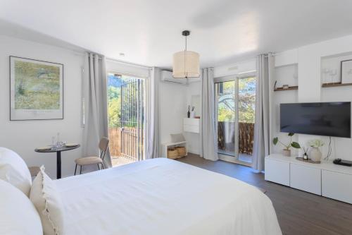 a white bedroom with a large bed and a tv at Studio lumineux avec jardin privé et parking in La Turbie