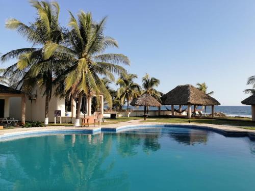 a swimming pool at a resort with palm trees and the ocean at Hotel & Resort Casa Bella in El Hawaii