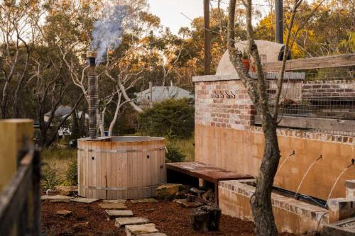 a wooden bench next to a barrel and a tree at Harvest Cottage Blue Mountains in Leura