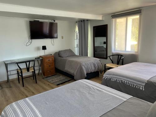 a bedroom with two beds and a desk with a television at Hostal Doñihue in Doñihue