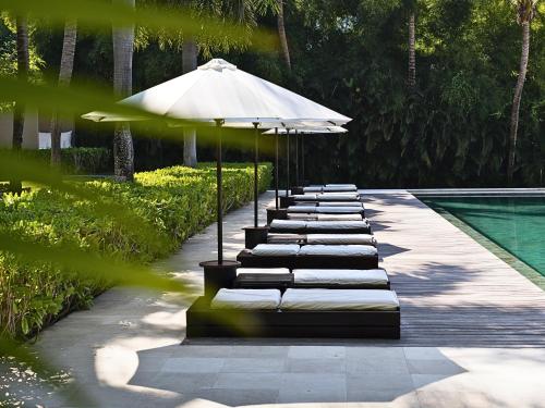 a row of lounge chairs with an umbrella next to a pool at 5-Star Boutique Hotel The Lombok Lodge in Tanjung