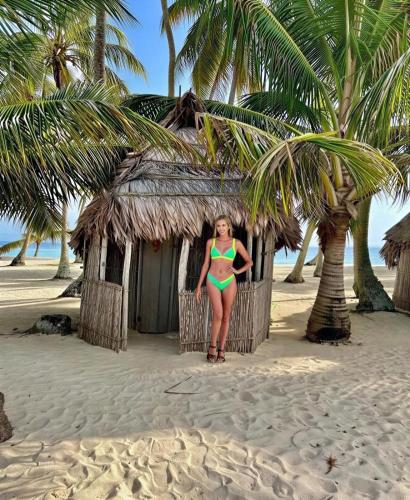 a woman in a bikini standing in front of a shack on the beach at Islas de Guna Yala Cabaña tradicional Guna Tubasenika in Arritupo Número Dos