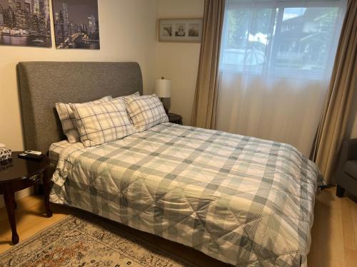 a bedroom with a bed with a plaid blanket and a window at Cozy Escape in the City in Port Coquitlam