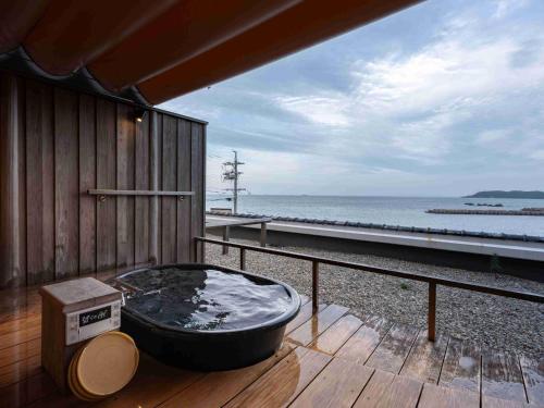 a hot tub sitting on a deck next to the ocean at Hamabenoyado Kameya in Toba