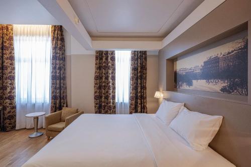 a hotel room with a large white bed and a chair at Opera Hotel in Riga
