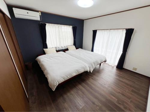 a bedroom with a bed with white sheets and two windows at アザミヴィラ青島 in Miyazaki