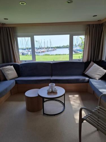 a living room with a blue couch and a table at Stacaravan met schitterend uitzicht over het meer, in Friesland! Op de 5-sterren Camping de Kuilart met Zwembad! in Koudum
