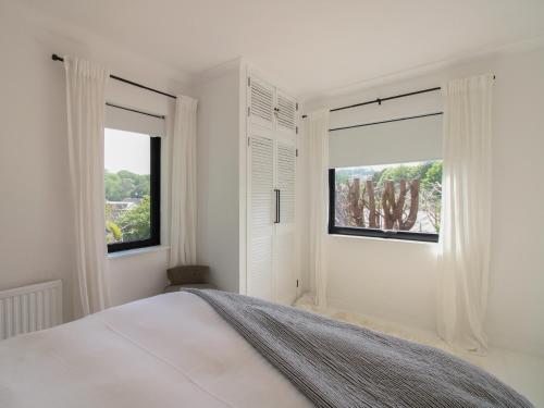 a white bedroom with a large bed and two windows at West Island in Kingsbridge
