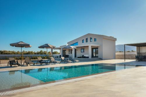 a swimming pool with chairs and umbrellas in front of a house at Villa Samantha - Private Pool, 3 Ensuite Bedrooms & Complete Privacy near Laganas, By TK Premium Stays in Ambelókipoi