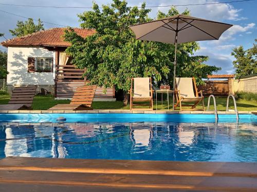 a pool with two chairs and an umbrella at ZOĆEVIĆA KONAK in Petrovići