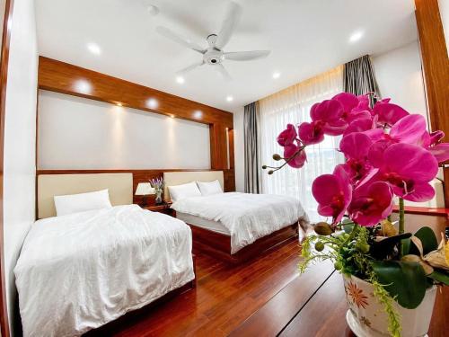 a bedroom with two beds and a vase with pink flowers at Pandora Hotel Cần Thơ in Can Tho