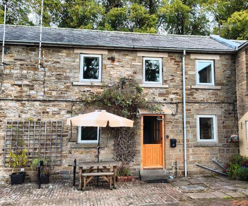 a stone house with an orange door and an umbrella at Mews Cottage in Middleton in Teesdale