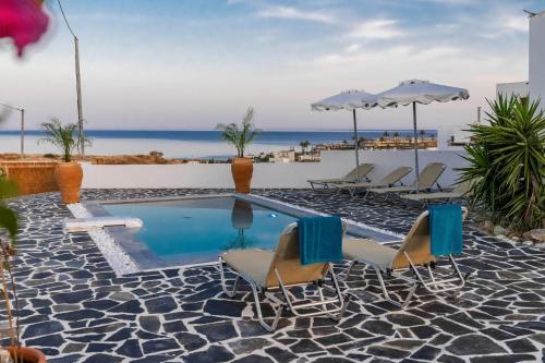 a pool with chairs and umbrellas and the ocean at Cosy House in Kiotari with Garden and Terrace in Kiotari