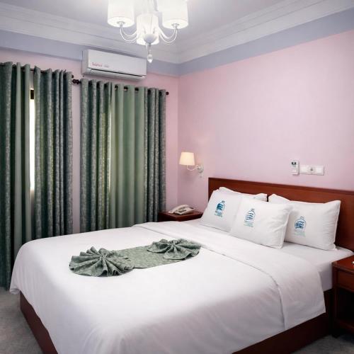 a bedroom with a white bed with green curtains at Arenah hotel in Yaoundé