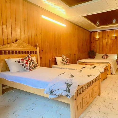 two beds in a room with wooden walls at The Royal Peaks in Kundālshai