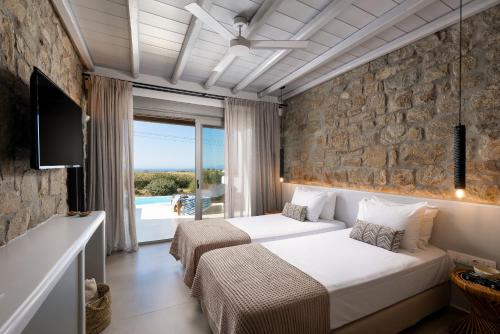 a bedroom with two beds and a stone wall at Aegean Hospitality in Mikonos