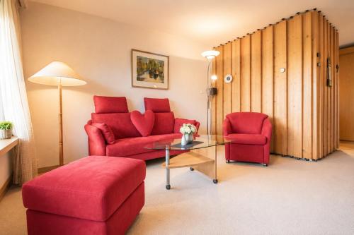 a living room with two red chairs and a table at Rehwiesa C24 - Alpenstudio mit Weisshornblick - Hallenbad-by Arosa Stay in Arosa