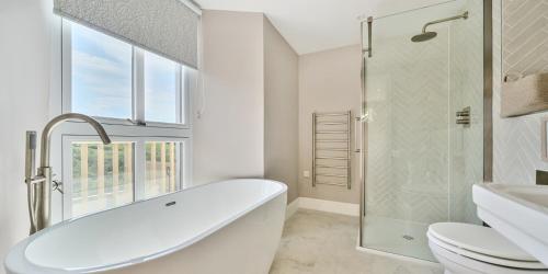 a white bathroom with a tub and a toilet at Brock's Beach House in Saint Gennys