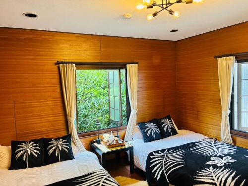 two beds in a room with wooden walls and a window at Airportside Chillhouse in Toyonaka