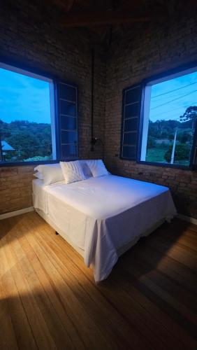 a bed in a room with two large windows at Casa 80 in Monte Belo