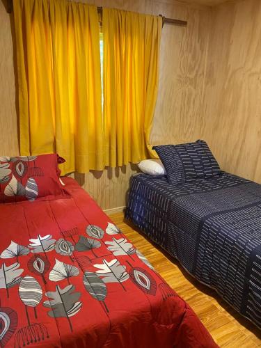 a bedroom with two beds and a window with yellow curtains at Cabaña Payer in Villarrica