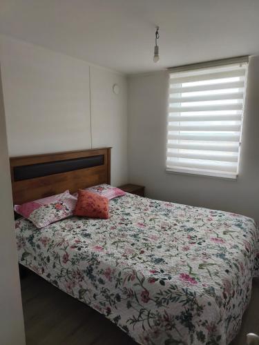 a bedroom with a bed with a floral comforter and a window at Departamento Temuco in Temuco