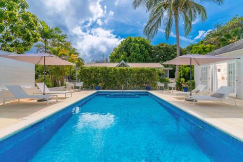 a pool with chairs and umbrellas next to a house at Gibbs Cottages in Saint Peter