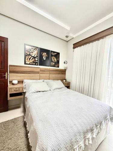 a bedroom with a white bed with a wooden headboard at Quarto 4V Joinville Costa e Silva perto Centro in Joinville