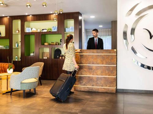 a woman pulling a suitcase in front of a man at Mercure Belfort Centre in Belfort