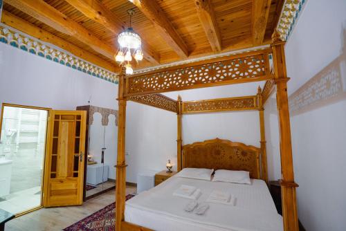 a bedroom with a wooden canopy bed with white sheets at Khalid Boutique in Bukhara