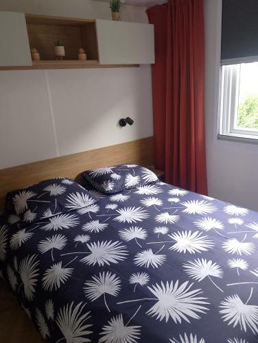 a bedroom with a bed with a blue and white comforter at Location mobil home in Litteau