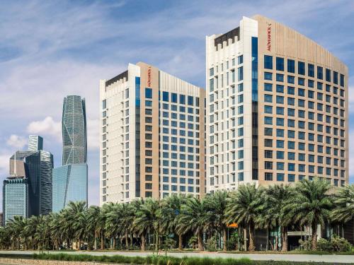 two tall buildings with palm trees in front of a city at Movenpick Hotel and Residences Riyadh in Riyadh