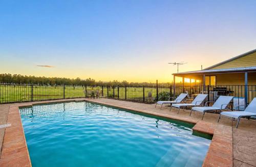 a swimming pool with chairs and a house at Stay at Shiraz in Pokolbin